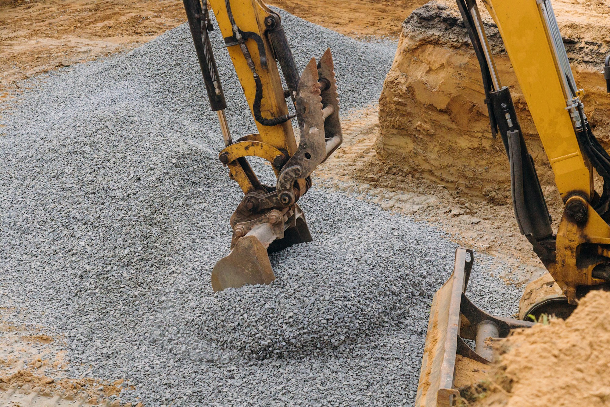 A yellow excavator moving gravel in the foundation in the house poles on gravel