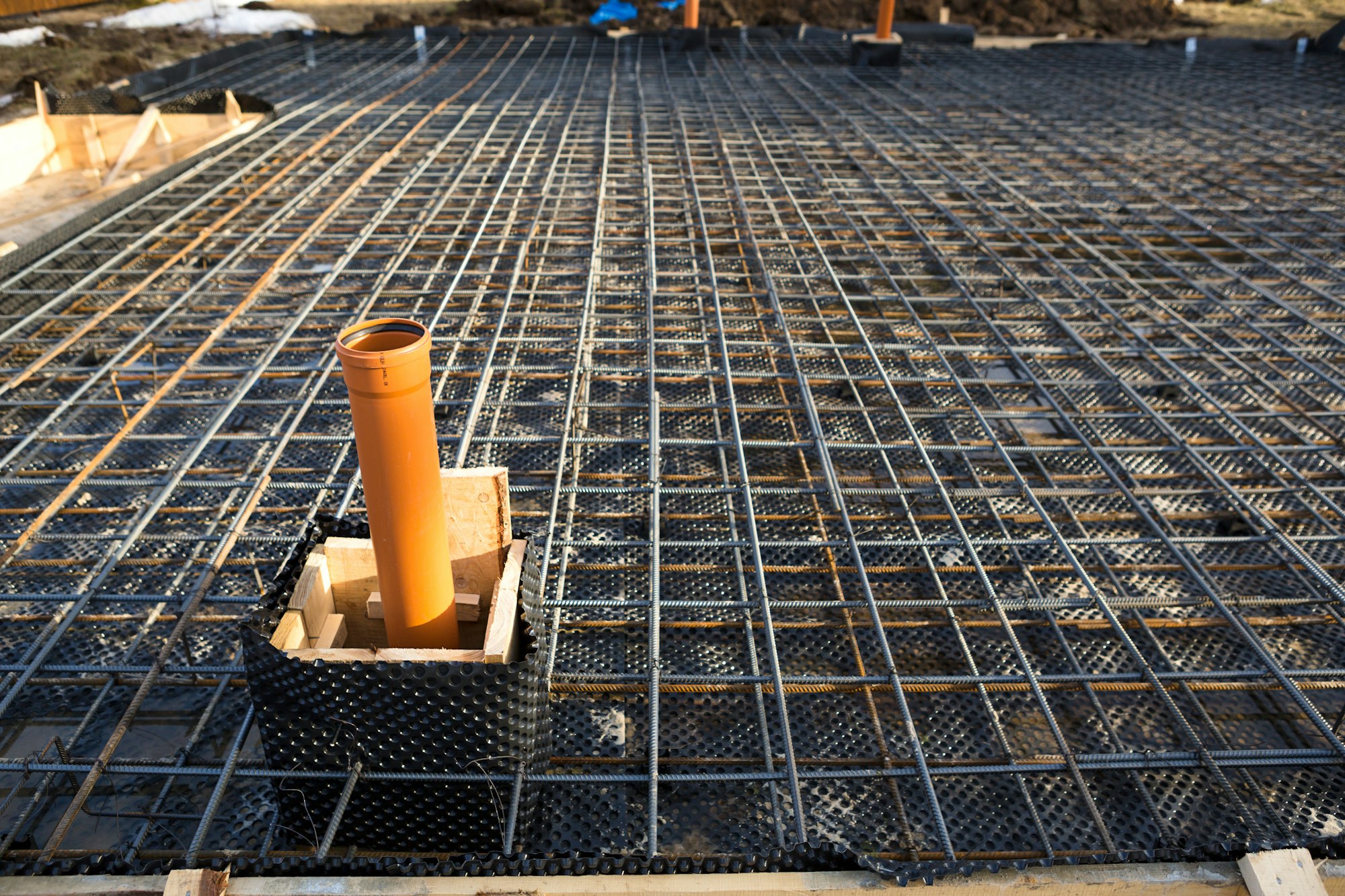 Iron fittings on a wooden blind area with laid pipes are the basis for pouring the foundation